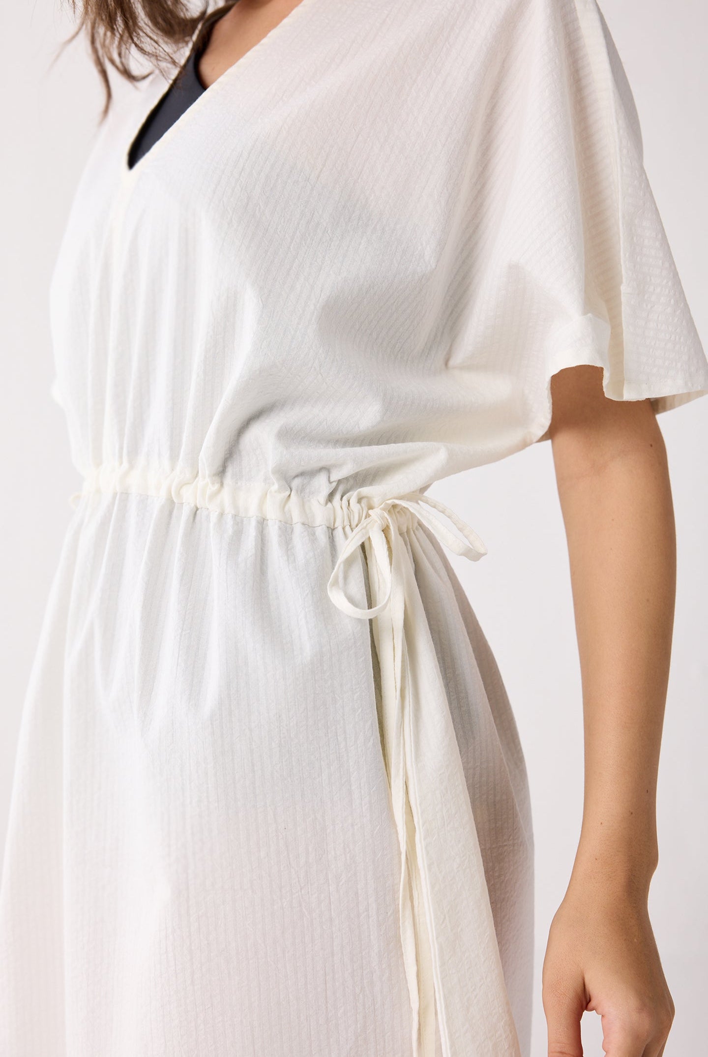 White cover up with a tie waist on a plain background