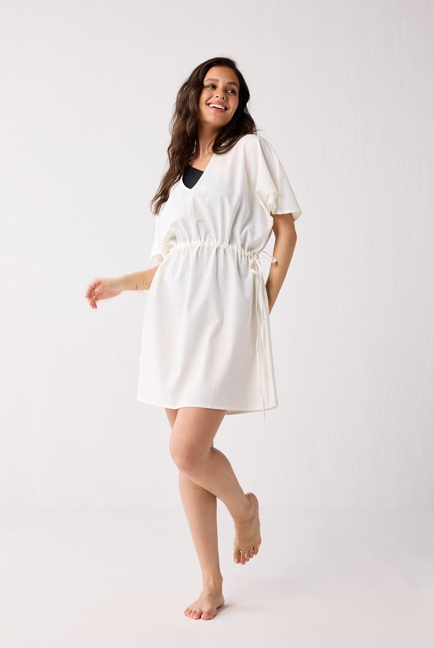 Woman wearing a white cover up on a plain background