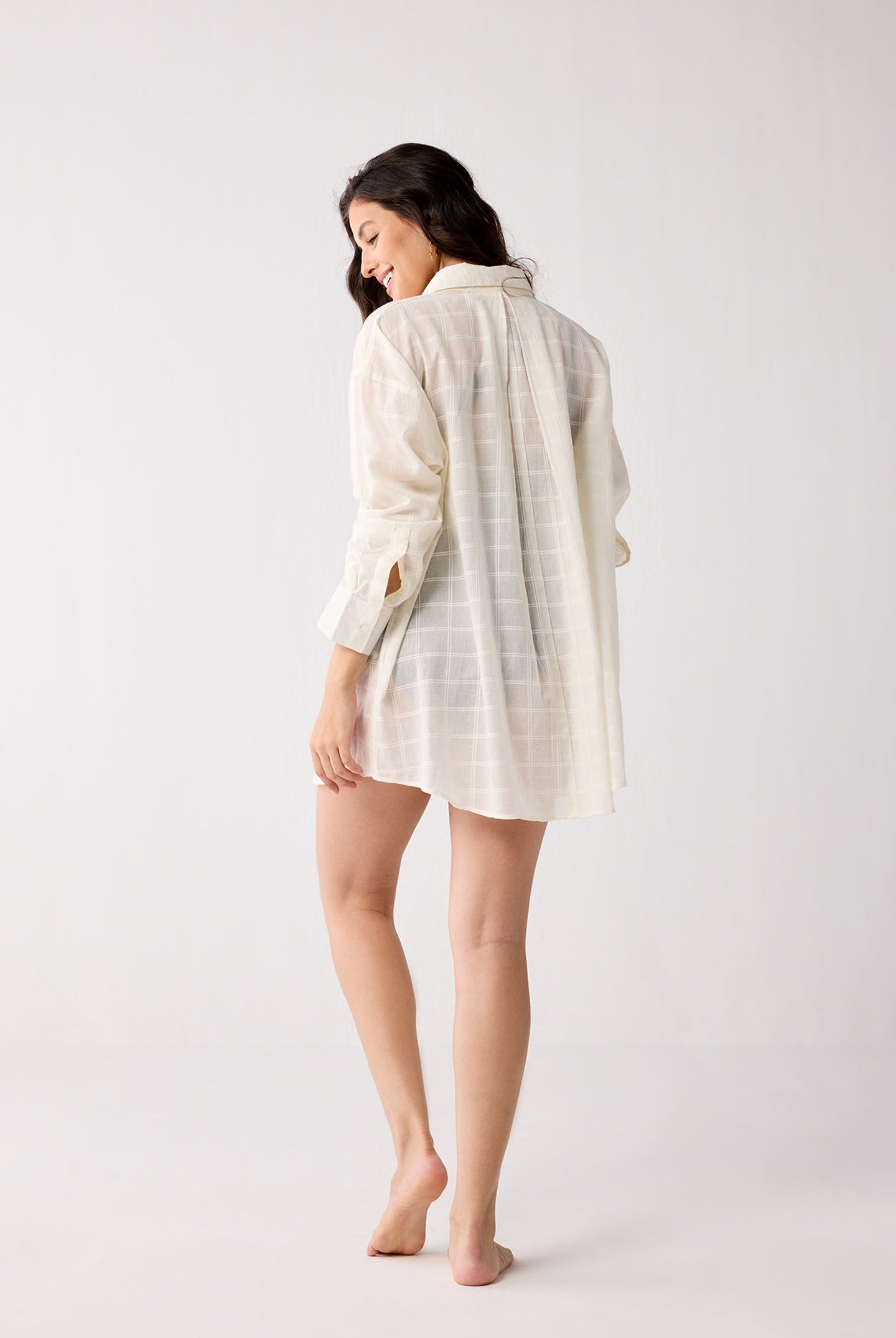 Woman wearing a white checkered shirt and shorts on a plain background