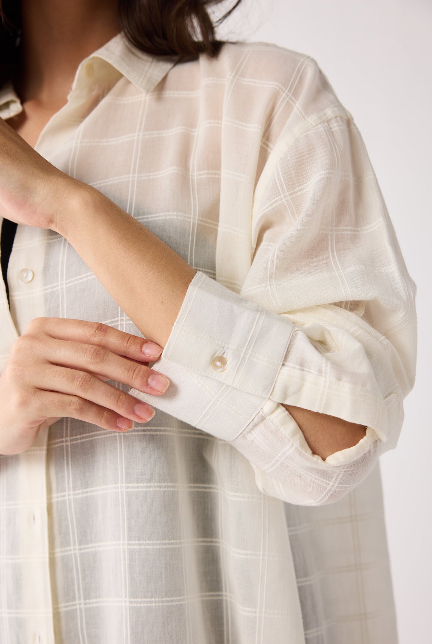 Person wearing a light-colored checkered shirt with rolled-up sleeves on a white background