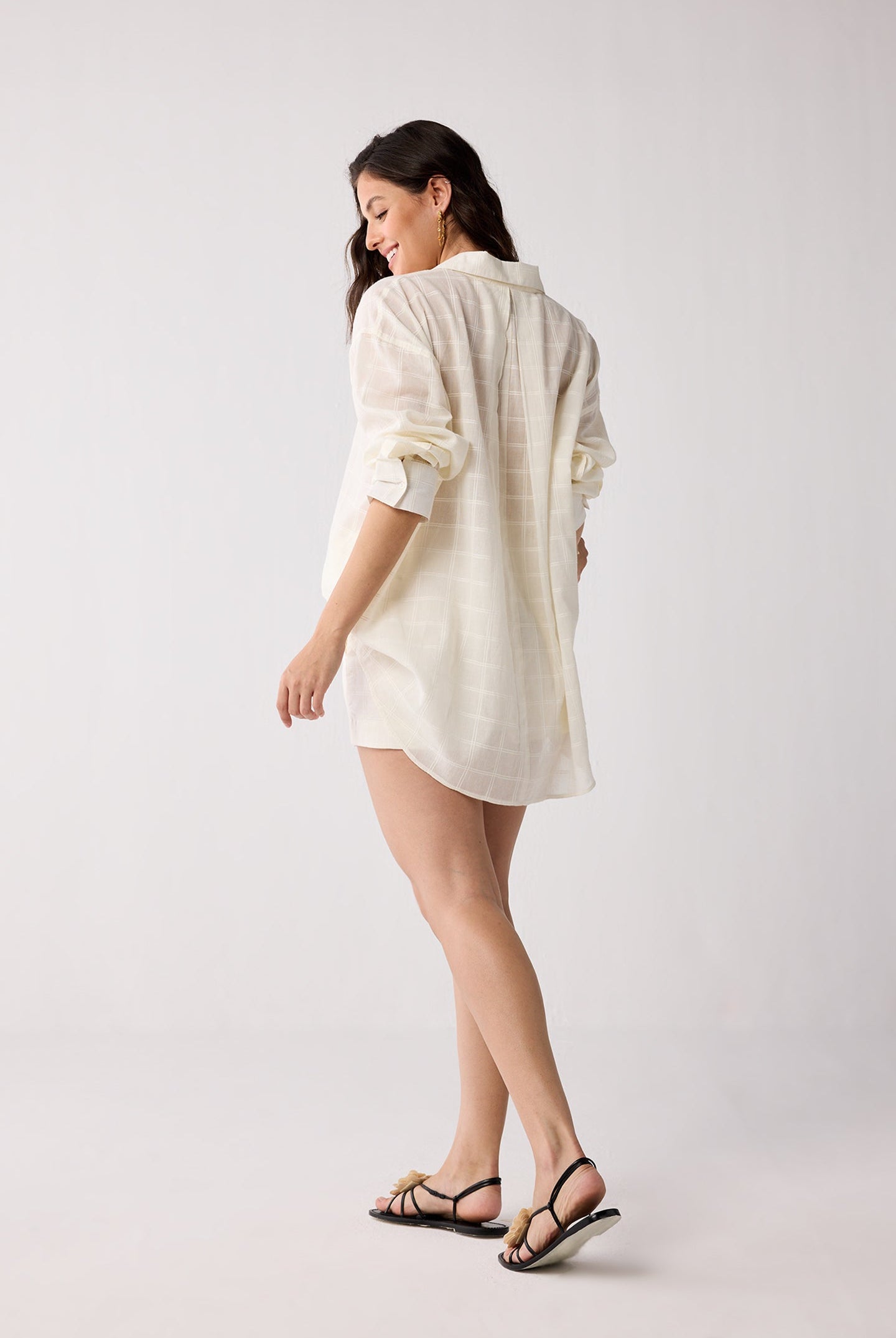 Woman wearing a white cover up with rolled-up sleeves on a plain background