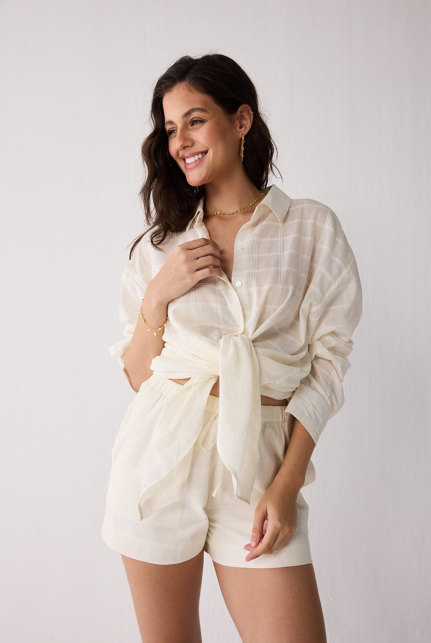 Woman wearing a white outfit with a tied shirt on a plain background