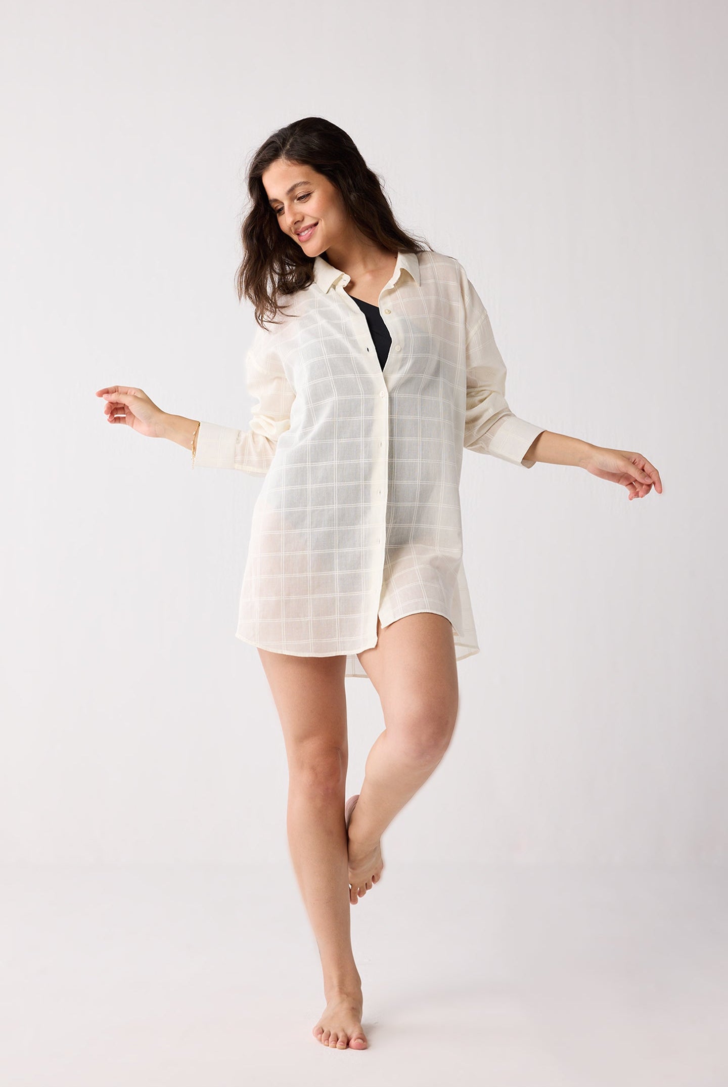 Woman wearing a white shirt over a black swimsuit on a white background