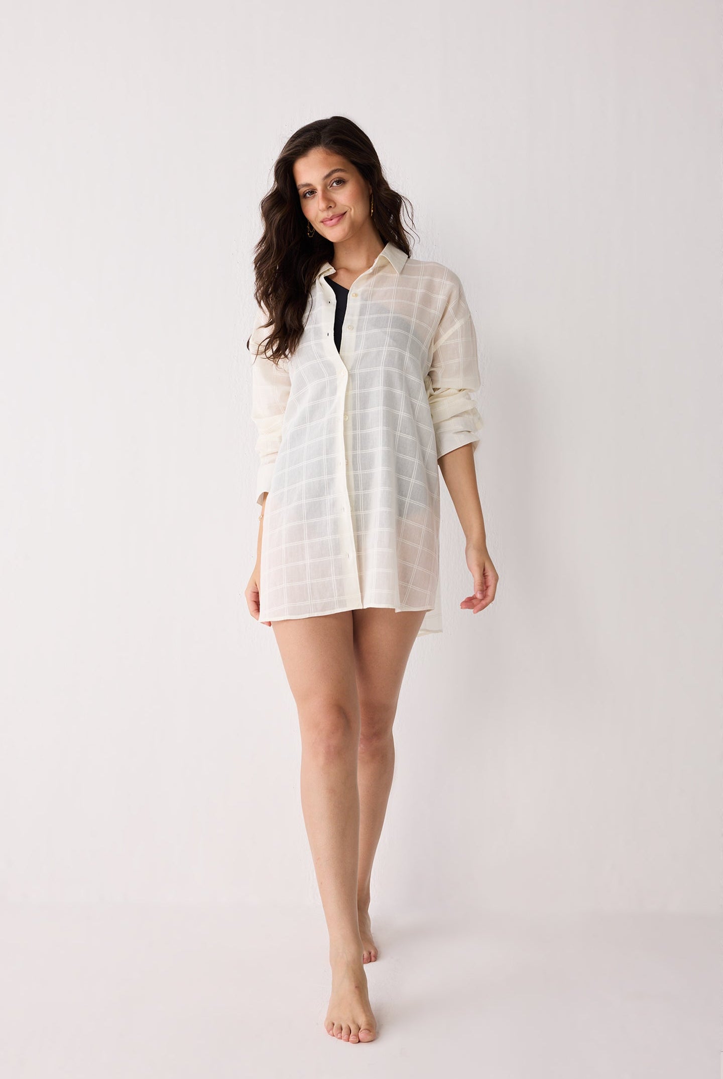 Woman wearing a white checkered shirt over a black swimsuit on a white background