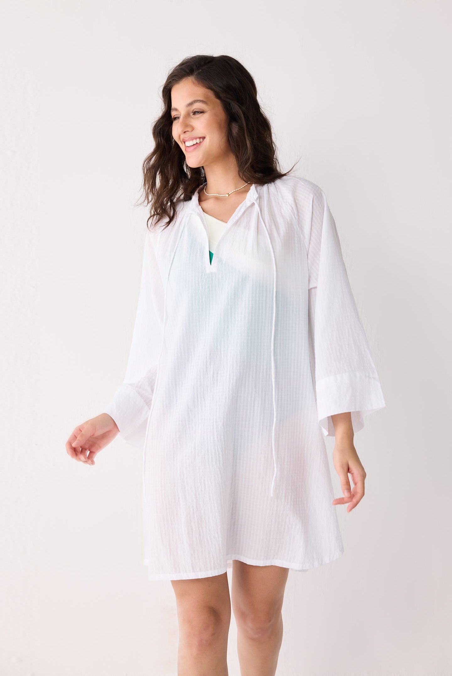 Woman wearing a white beach cover up with a plain background