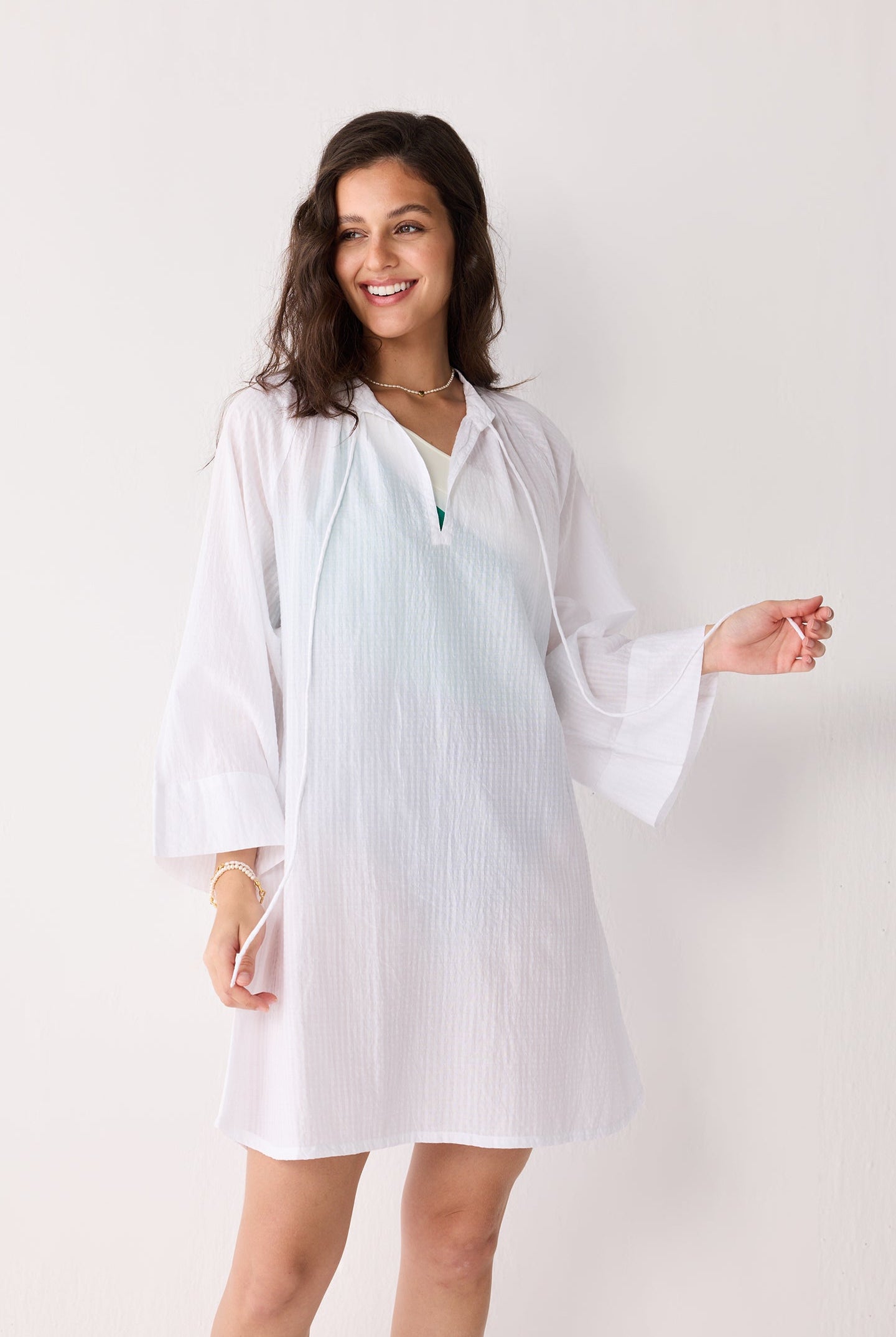 A woman wearing a white striped beach cover-up on a plain background