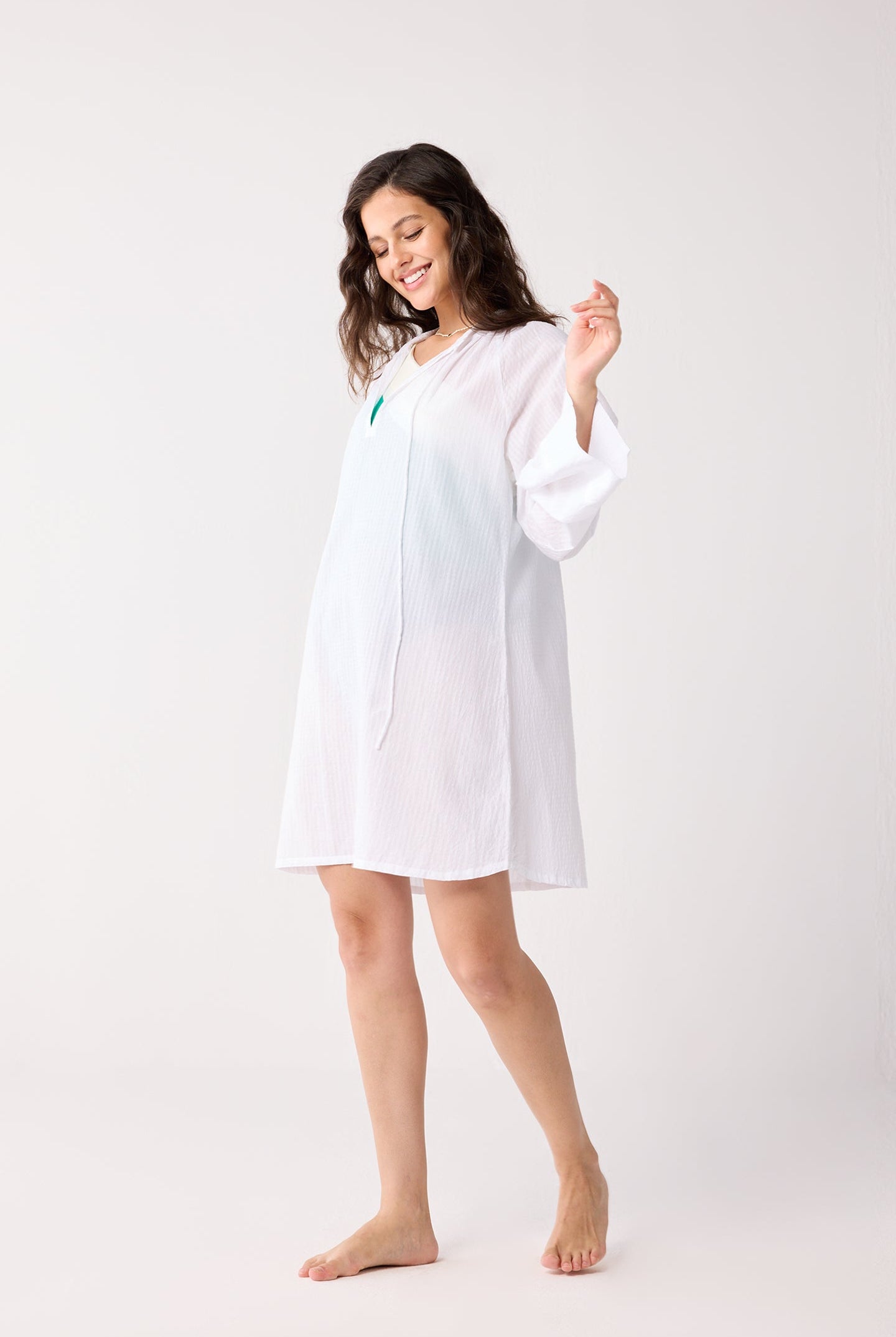 Woman wearing a white beach cover up on a plain background