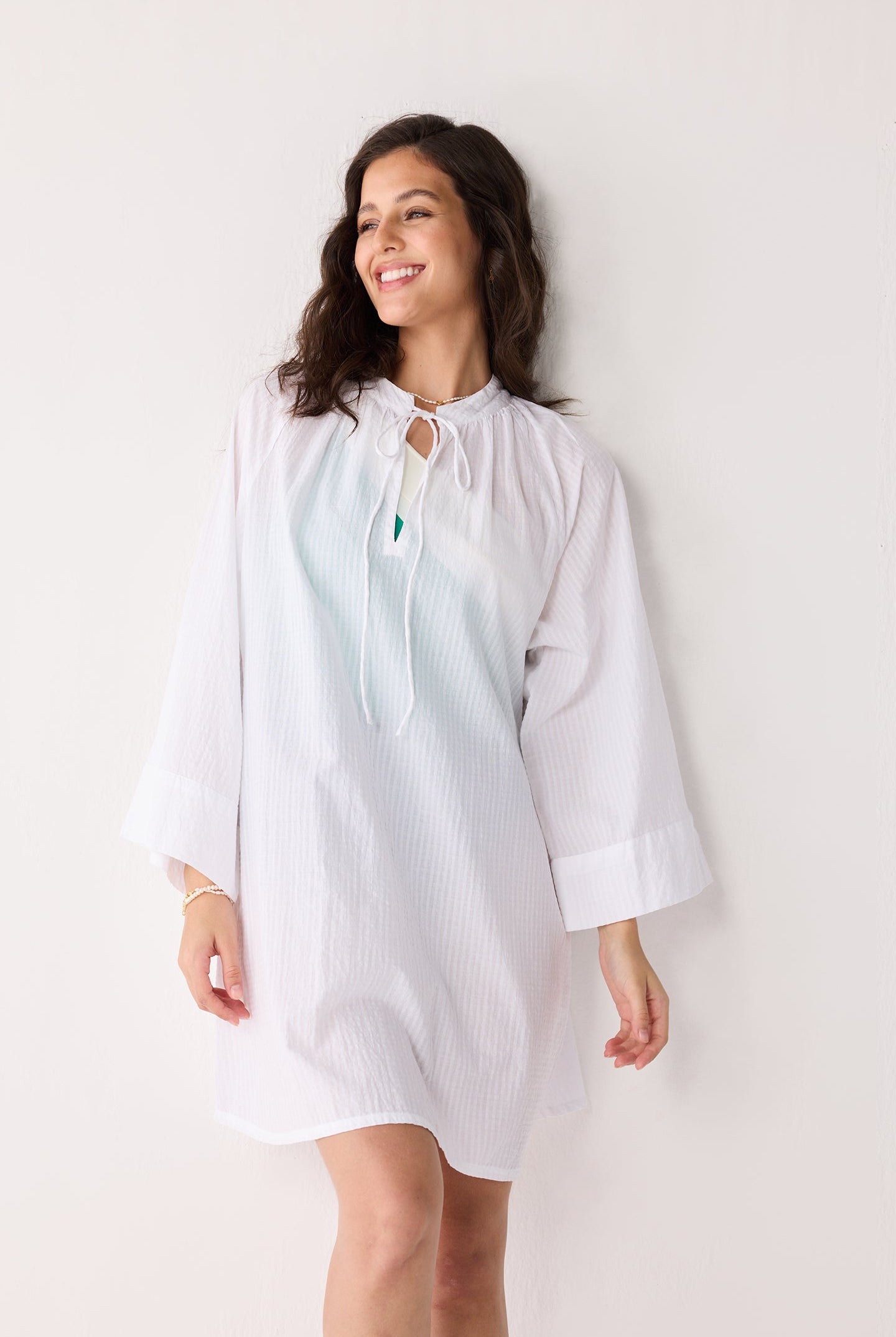 Woman wearing a light-colored cover up with a subtle pattern against a plain background