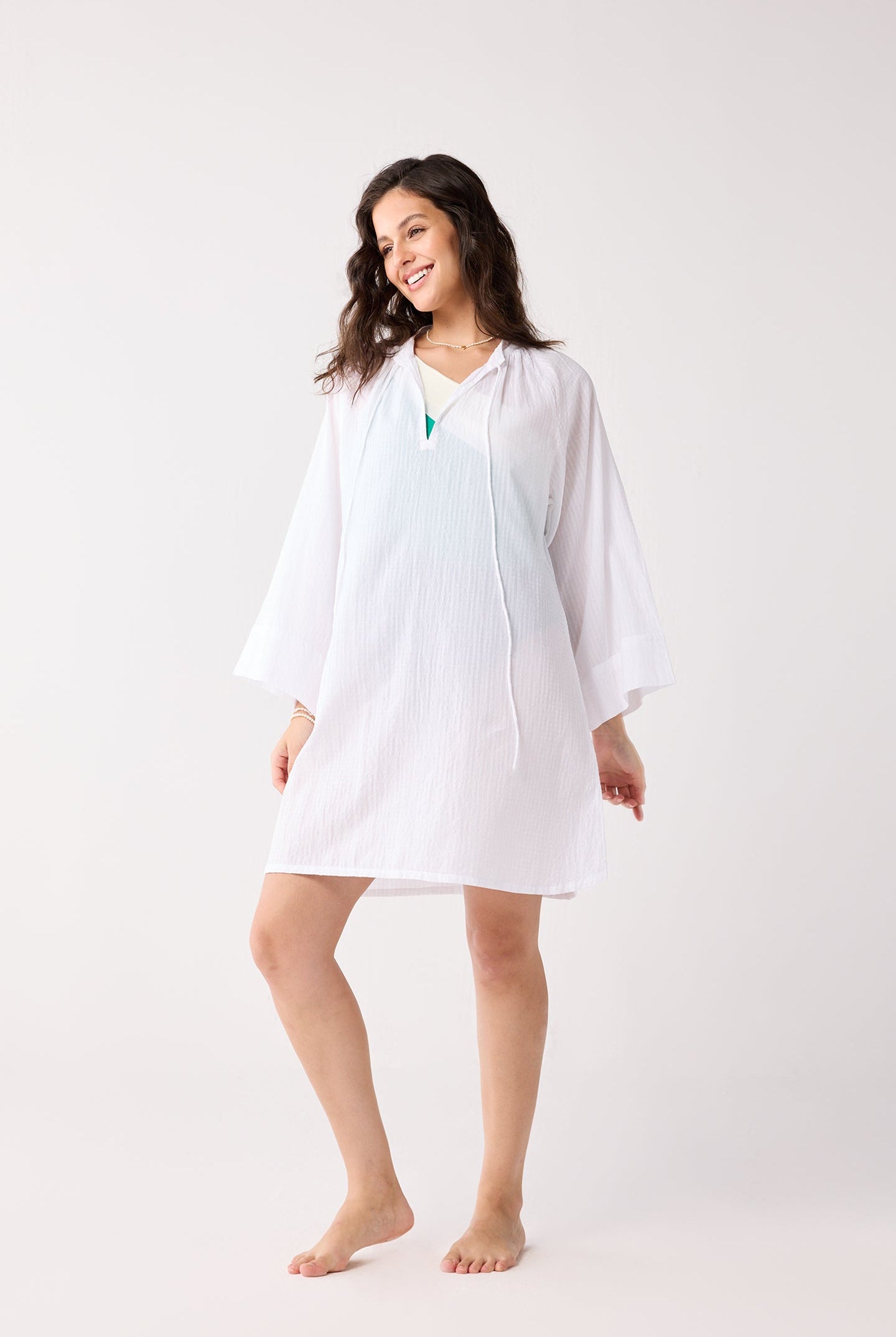 Woman wearing a white cover up on a plain background