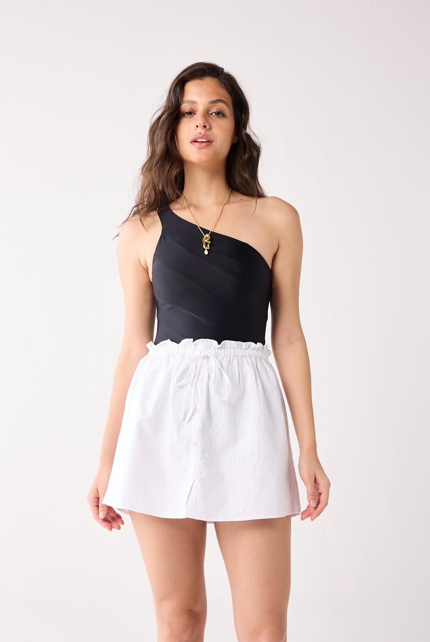 Woman wearing a black one-shoulder top and white skirt on a white background