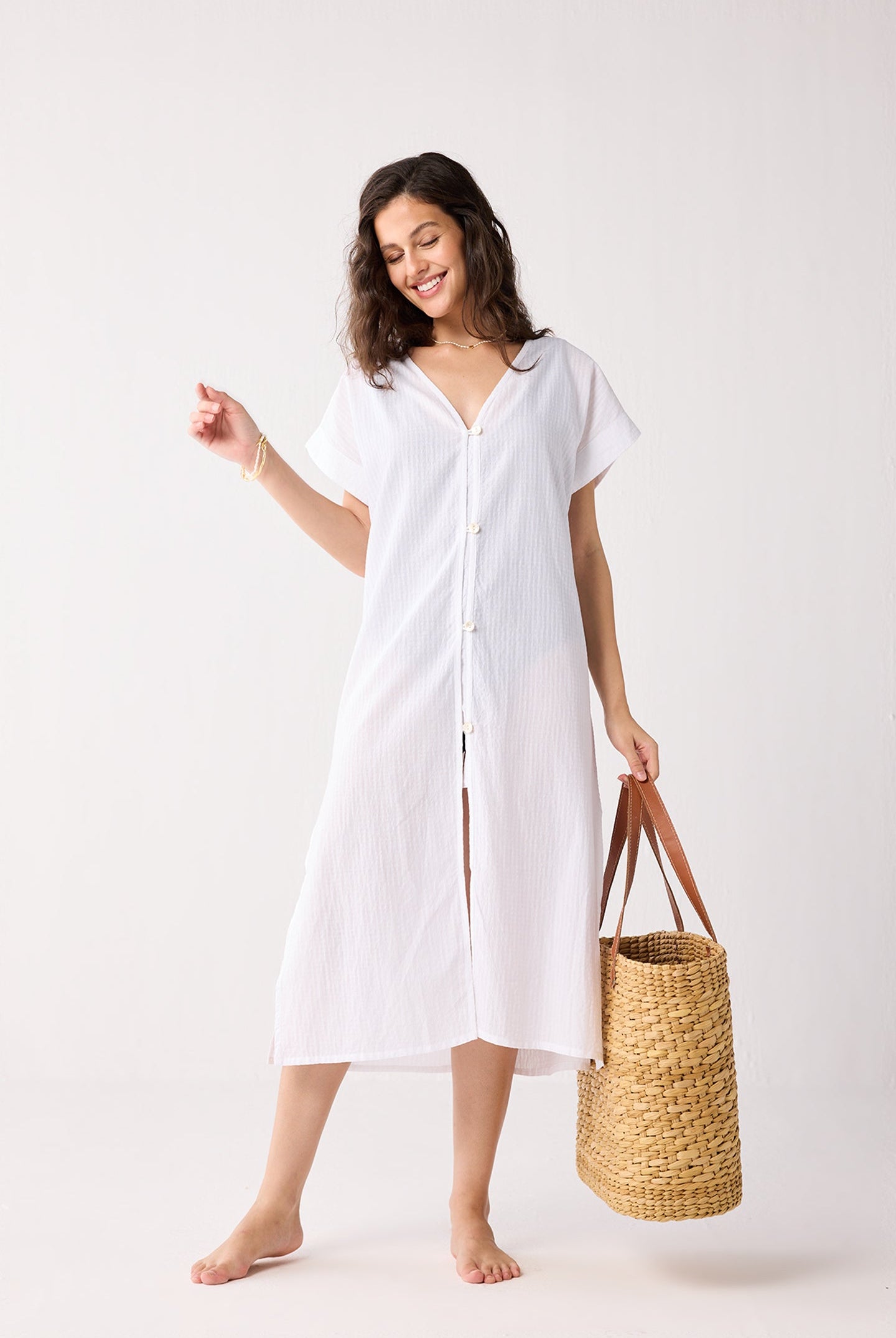 Woman wearing a white dress holding a woven bag on a white background