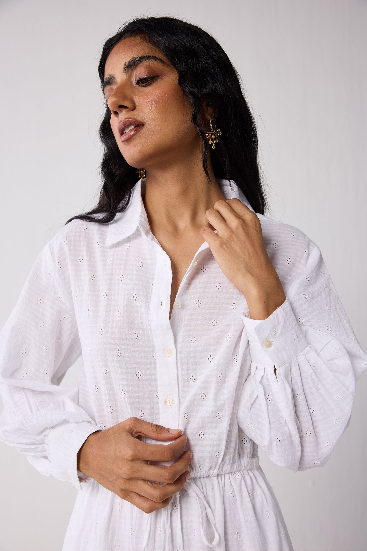 Woman wearing a white dress with a subtle pattern against a plain background