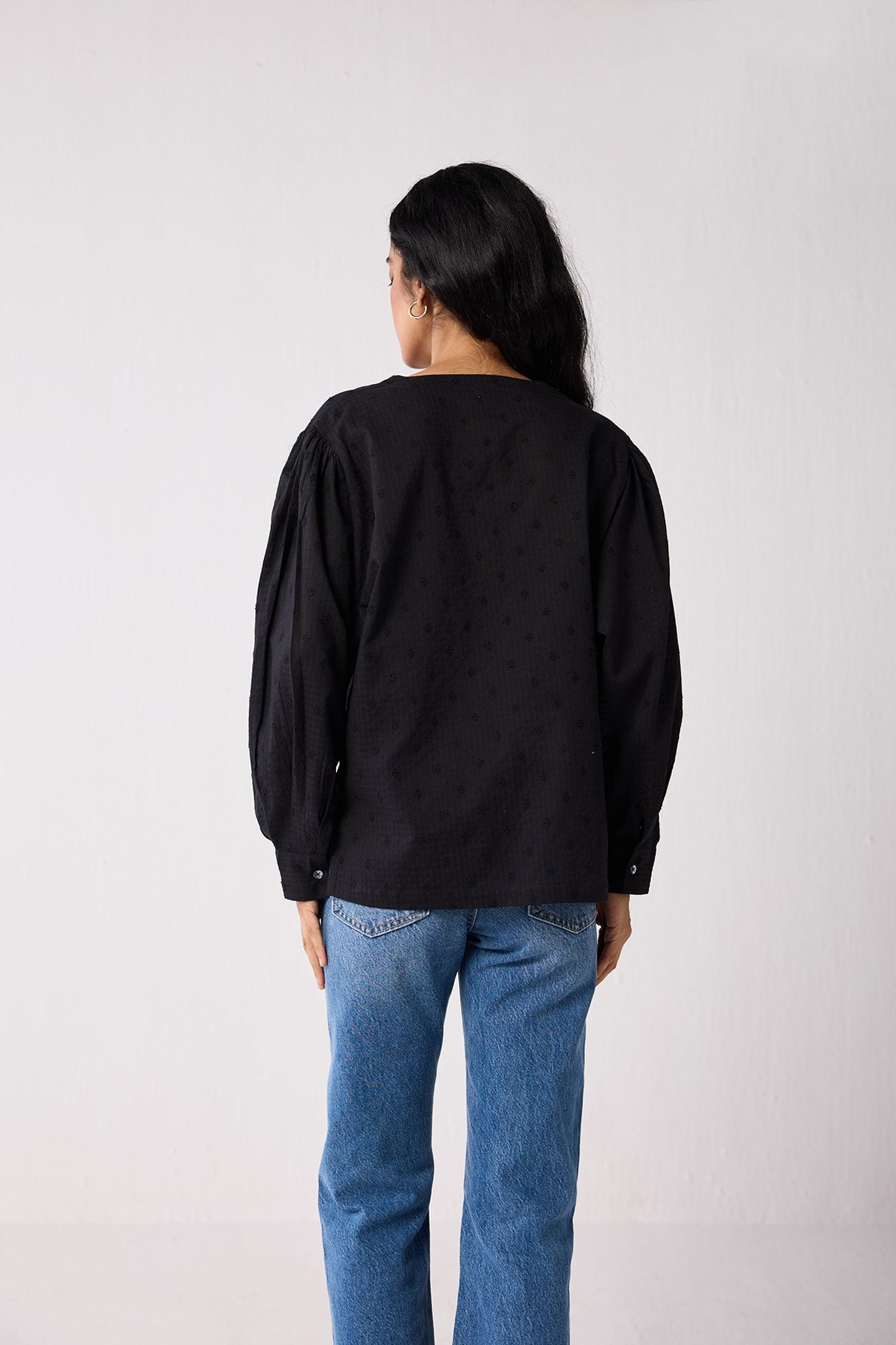Person wearing a black long-sleeve shirt and blue jeans on a white background