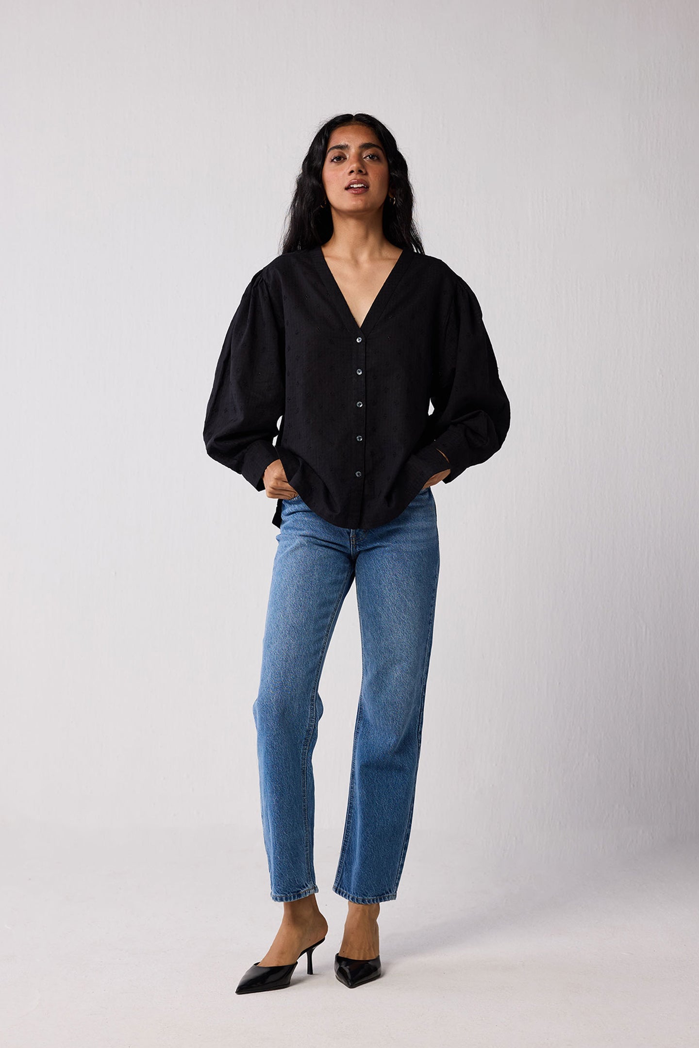 Woman wearing a black blouse and blue jeans against a white background