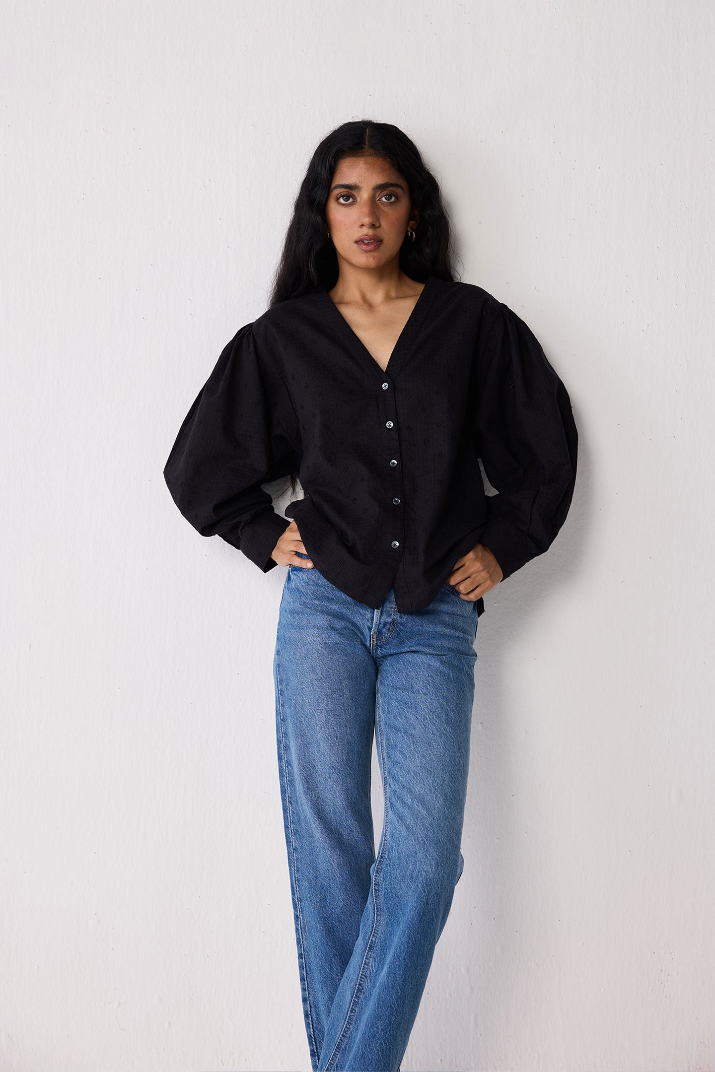 Woman wearing a black blouse and blue jeans against a white background