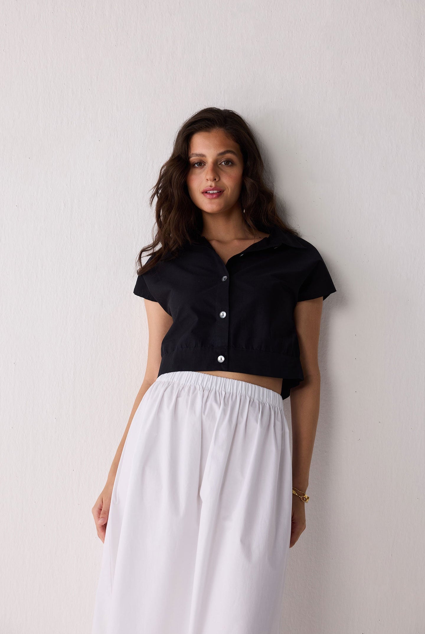 Woman wearing a black top and white skirt against a plain background