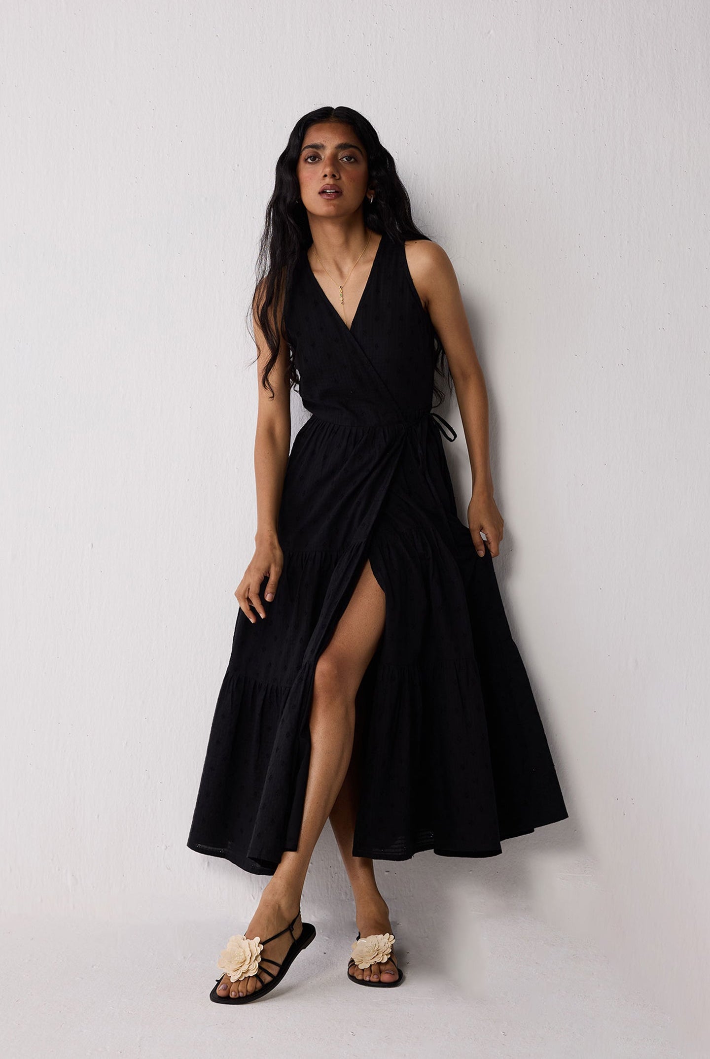 Woman wearing a black sleeveless dress with a slit on a plain background