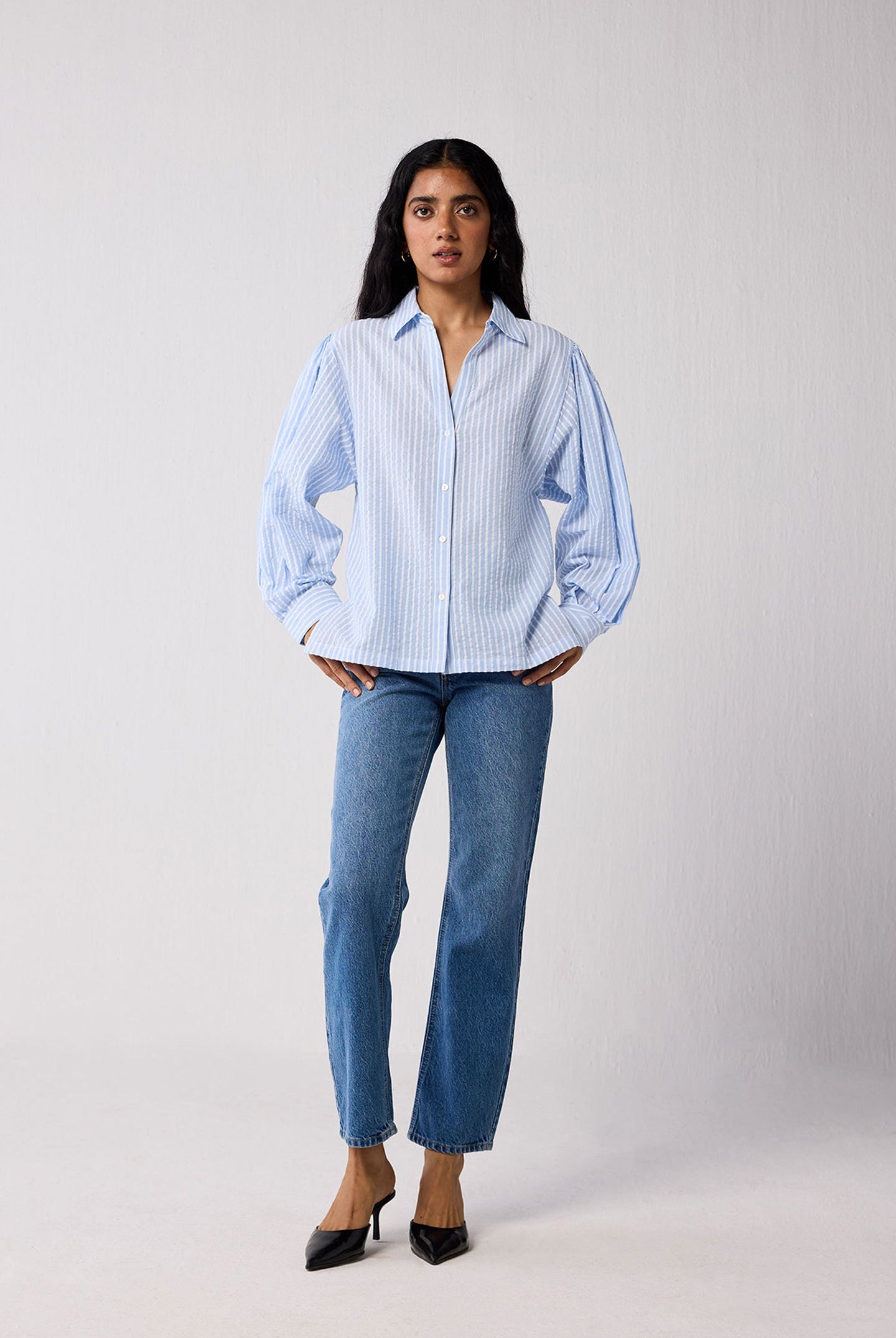 Woman wearing a light blue striped shirt and jeans on a white background