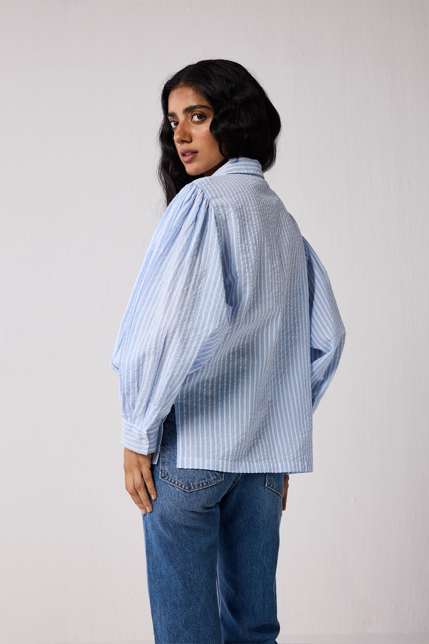 Woman wearing a light blue striped shirt and jeans on a white background
