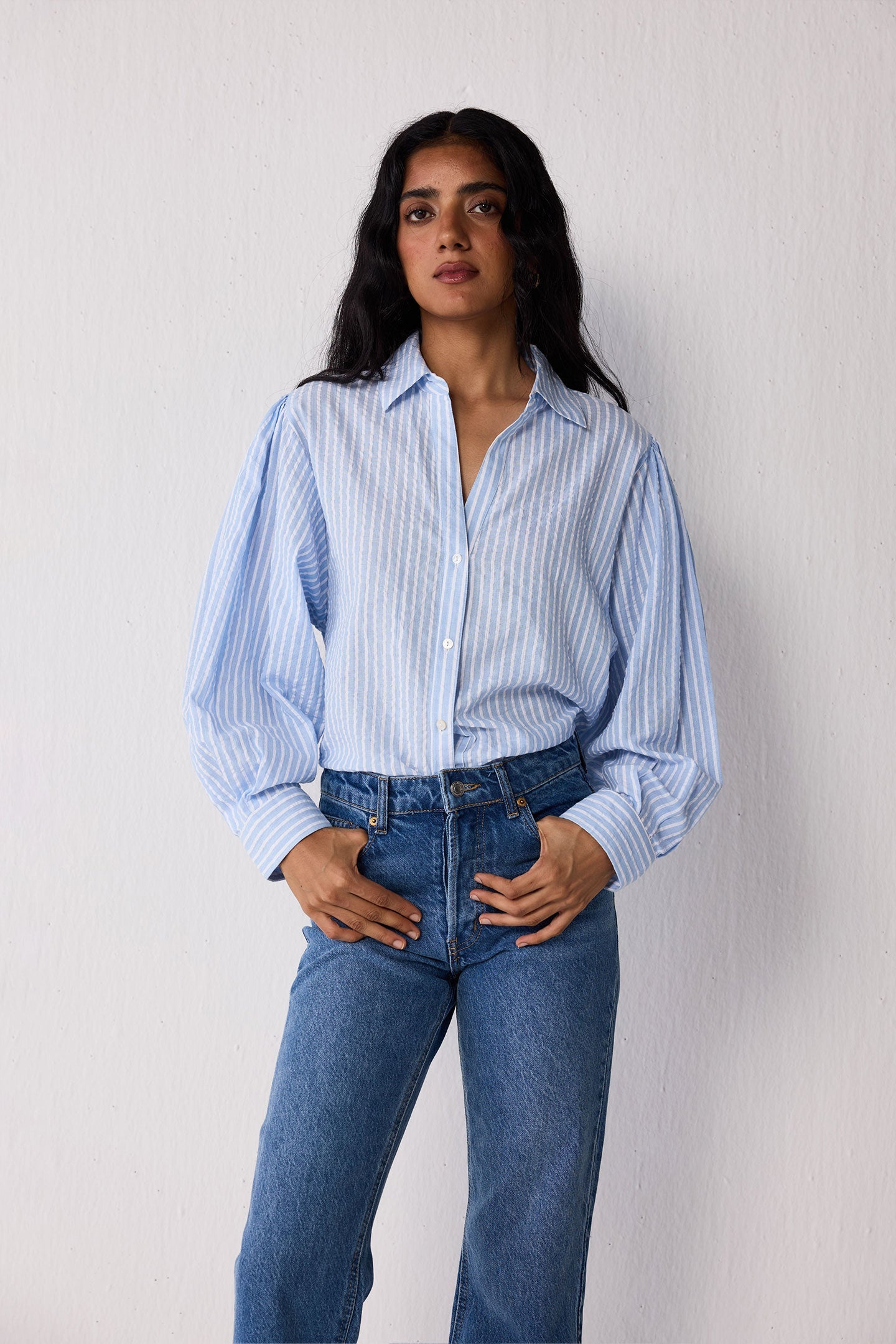 Woman wearing a light blue striped shirt and jeans on a white background