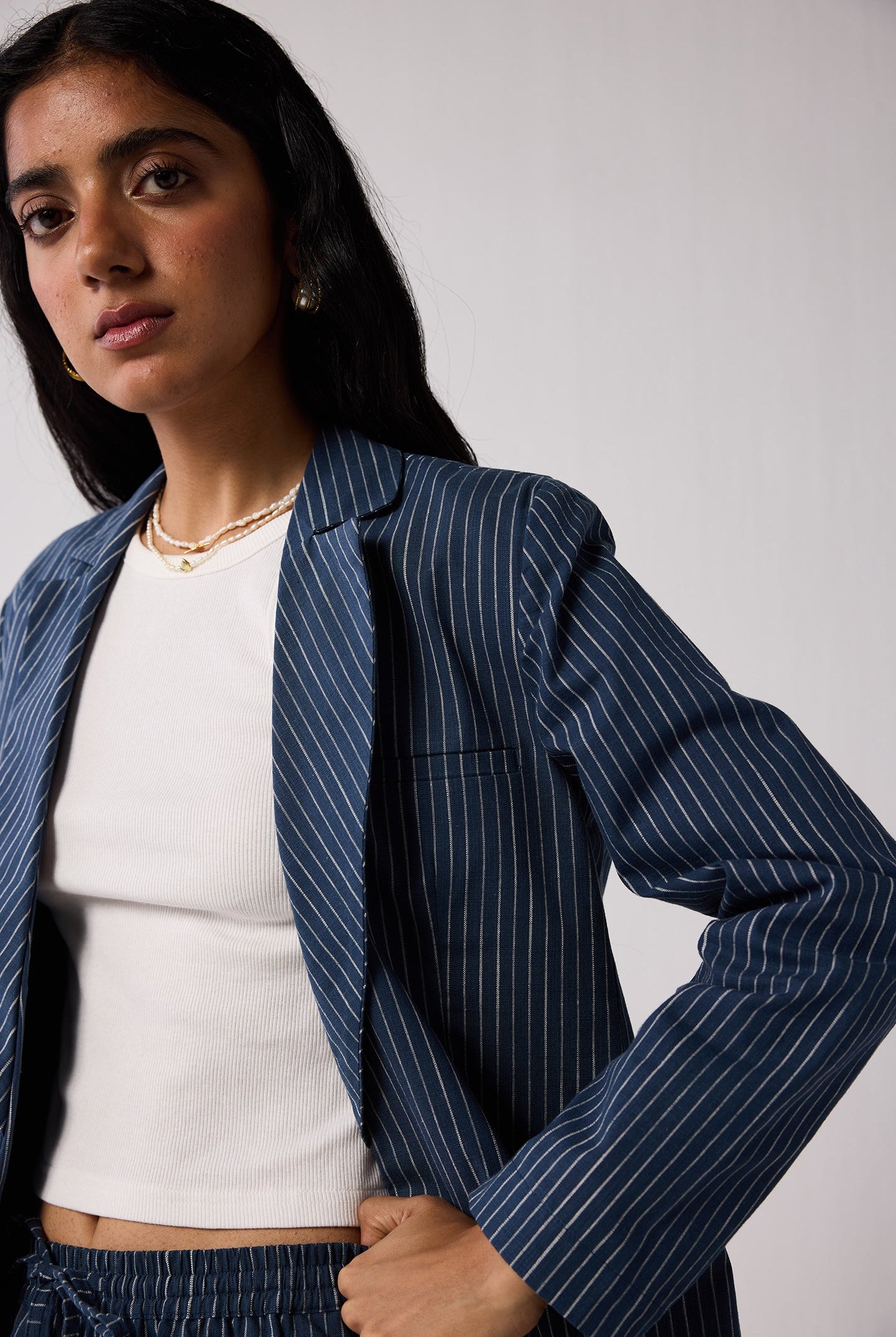 Woman wearing a blue pinstripe blazer over a white top against a plain background