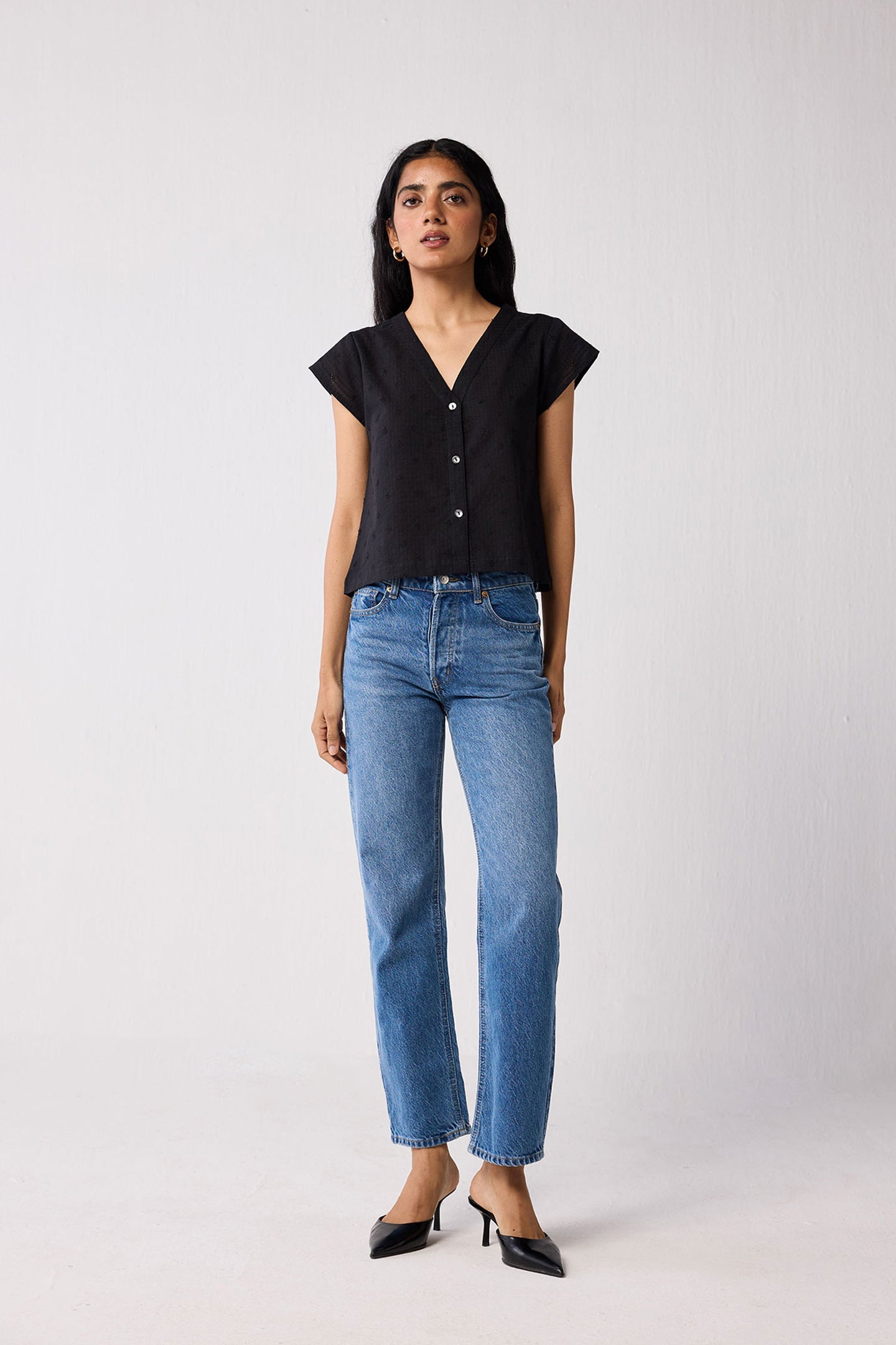 Woman wearing a black top and blue jeans on a white background