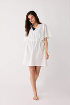 Woman wearing a white cover up with a belt on a plain background