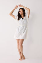 Woman wearing a white cover up on a plain background
