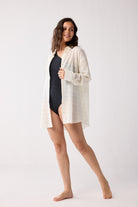 Woman wearing a white cover-up over a black swimsuit on a white background
