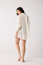 Woman wearing a white checkered shirt and shorts on a plain background