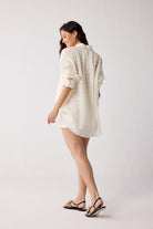 Woman wearing a white cover up with rolled-up sleeves on a plain background