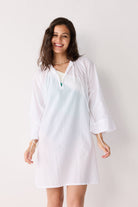 Woman wearing a white cover up against a plain background