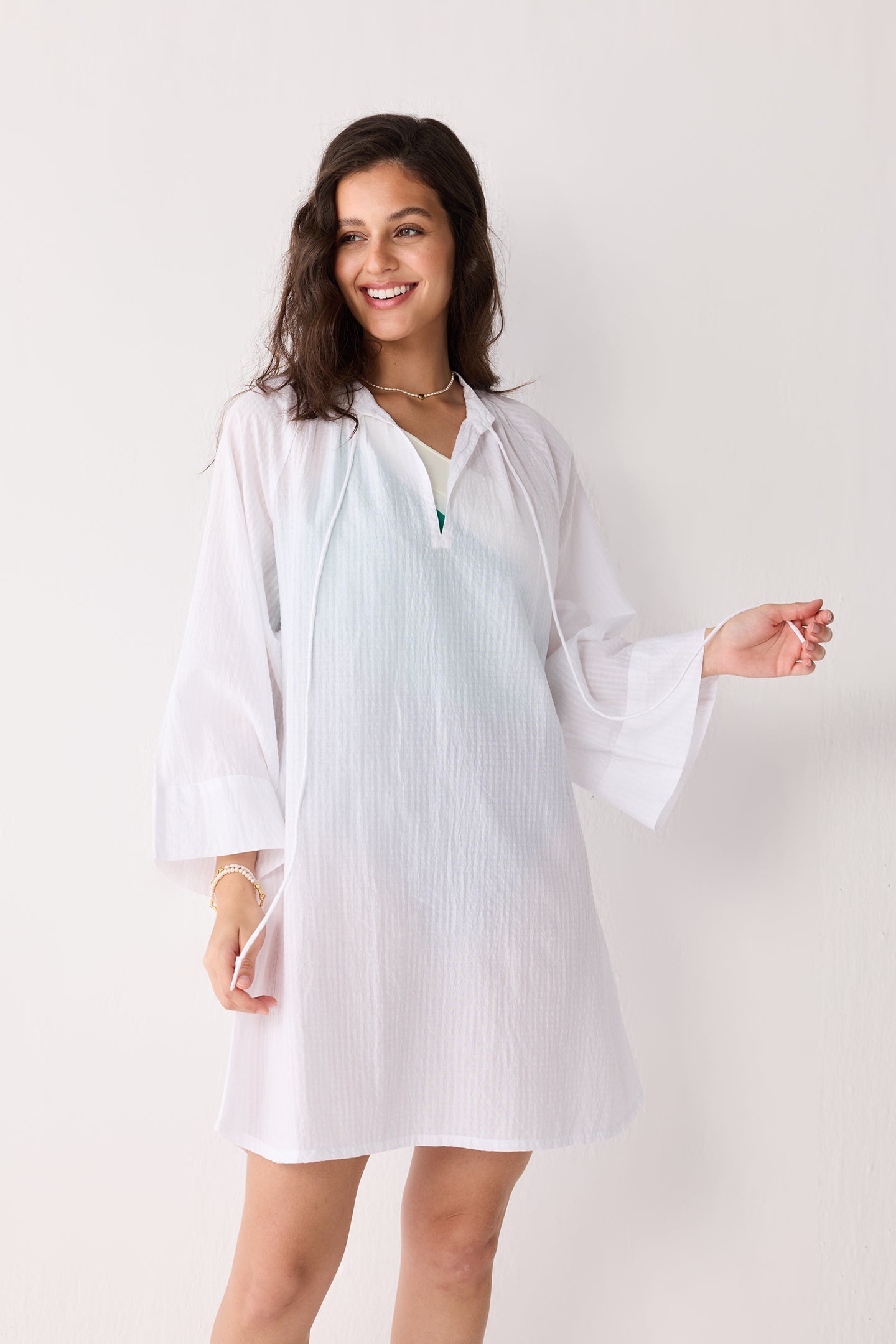 A woman wearing a white striped beach cover-up on a plain background