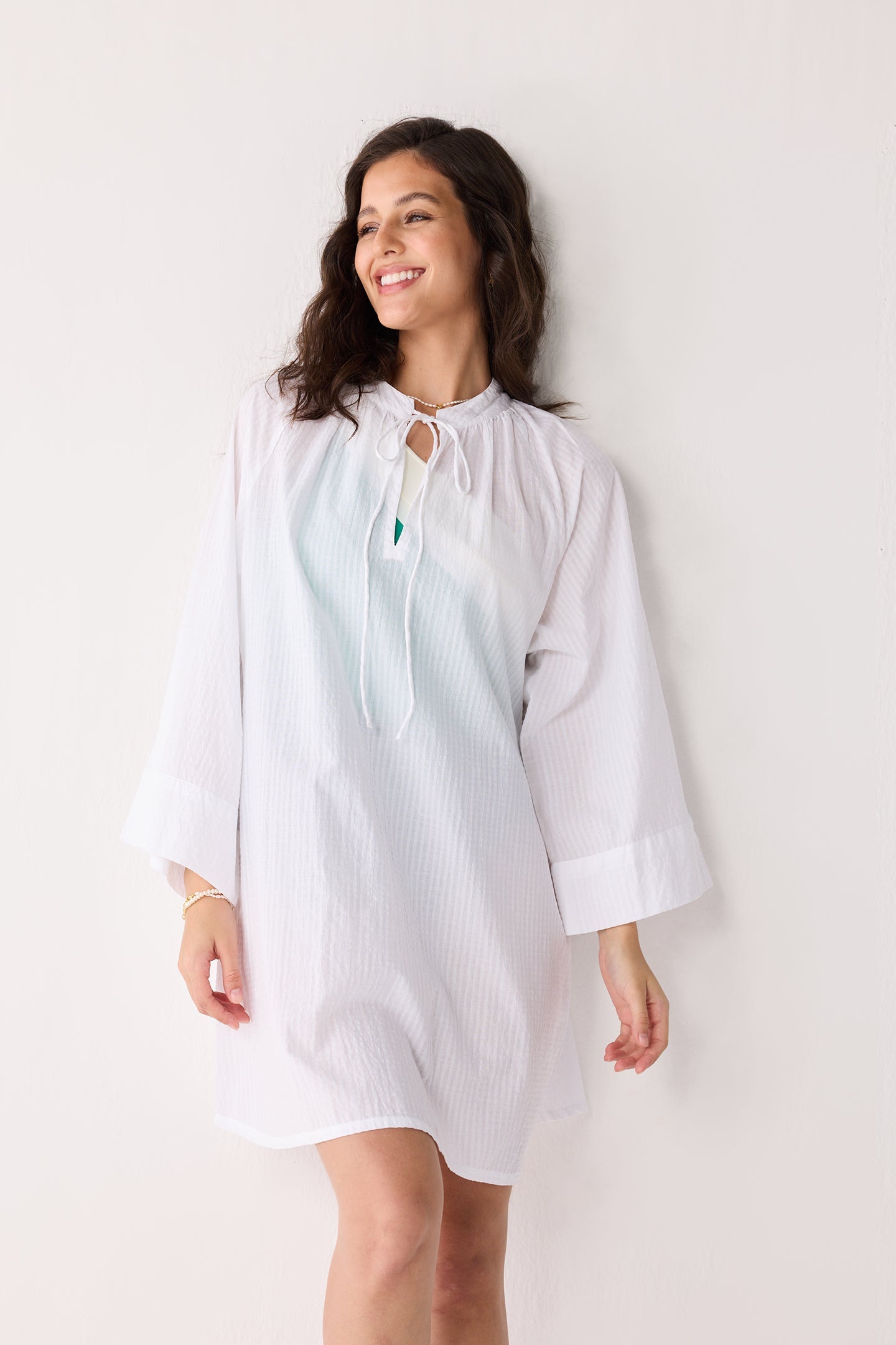 Woman wearing a light-colored cover up with a subtle pattern against a plain background