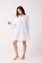 Woman wearing a white cover up on a plain background