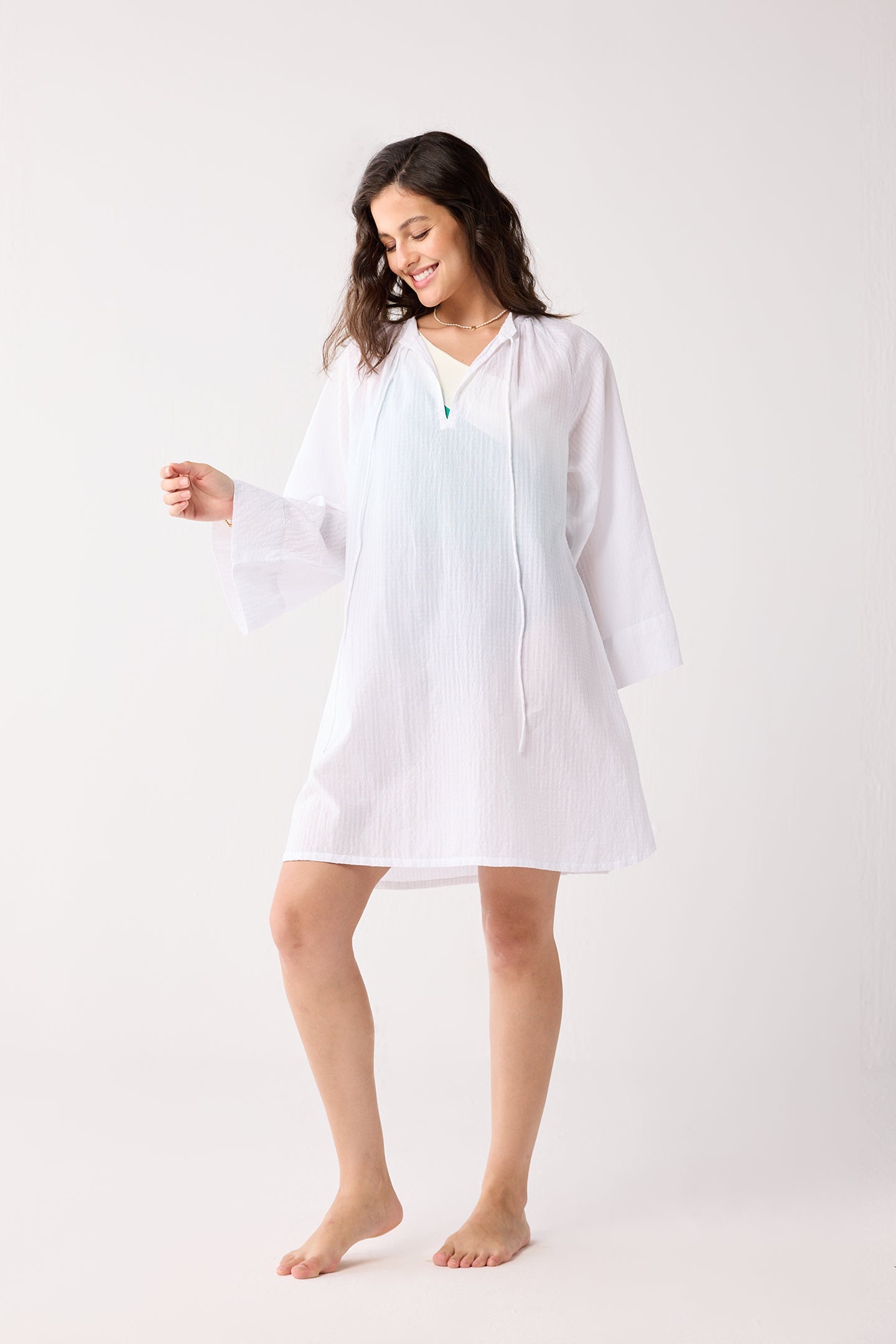 Woman wearing a white cover up on a plain background