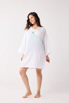 Woman wearing a white cover up on a plain background