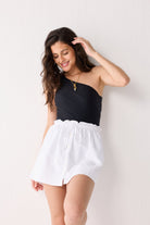 Woman wearing a black one-shoulder top and white shorts against a plain background