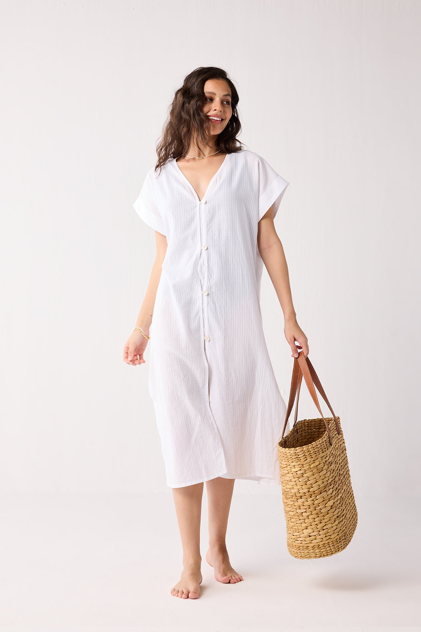 Woman wearing a white dress holding a woven bag on a white background