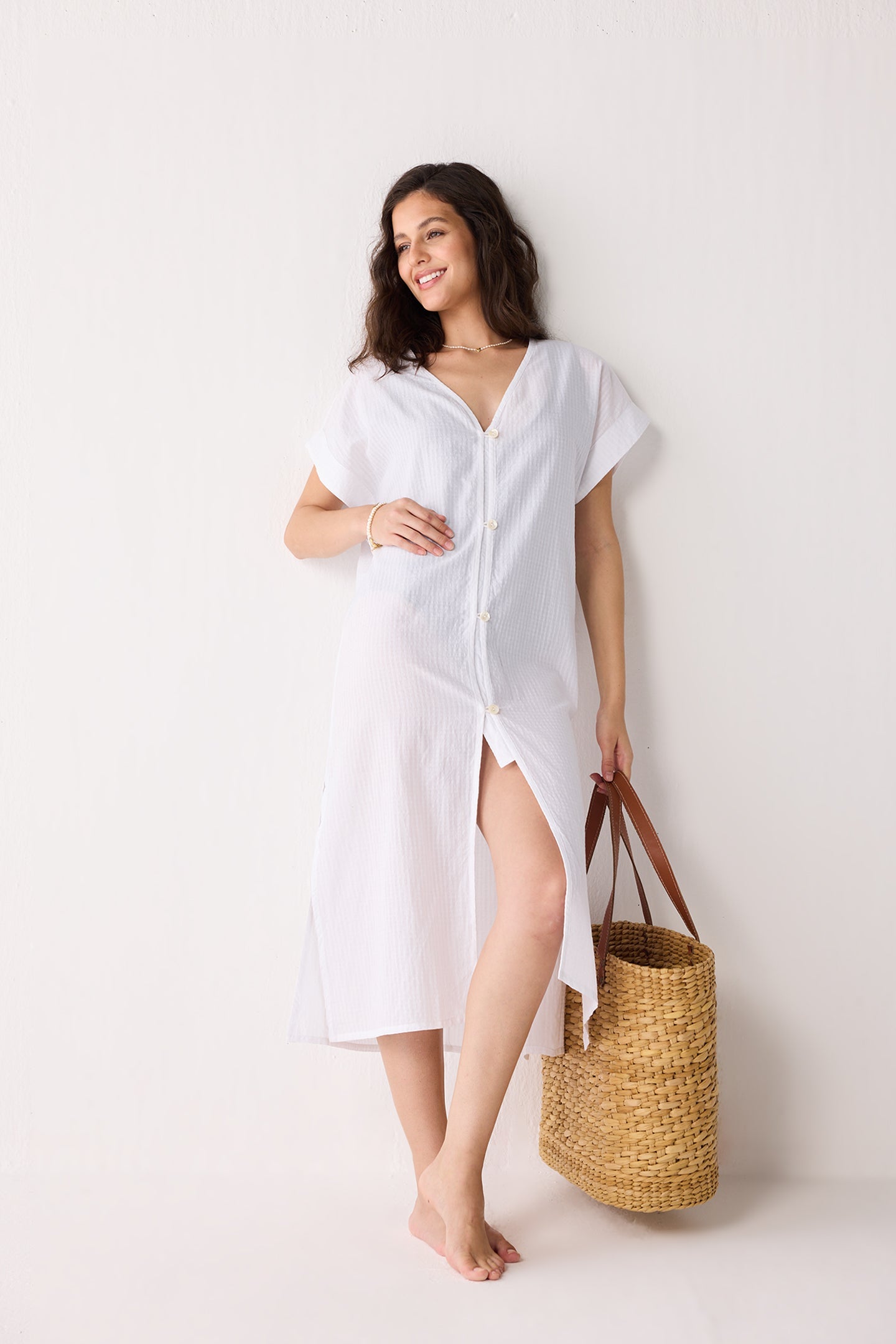 Woman wearing a white cover-up with a straw bag on a white background