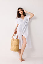 Woman in a white dress holding a woven bag against a white background