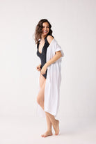Woman wearing a black swimsuit and white cover-up on a white background
