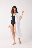 Woman wearing a black swimsuit and white cover-up on a white background