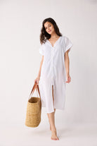 Woman wearing a white dress holding a woven bag on a white background