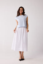 A woman wearing a light blue striped top and a white skirt on a plain background