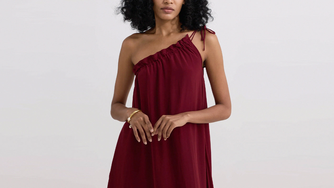 Woman wearing a burgundy one-shoulder dress on a plain background