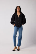 Woman wearing a black blouse and blue jeans against a white background