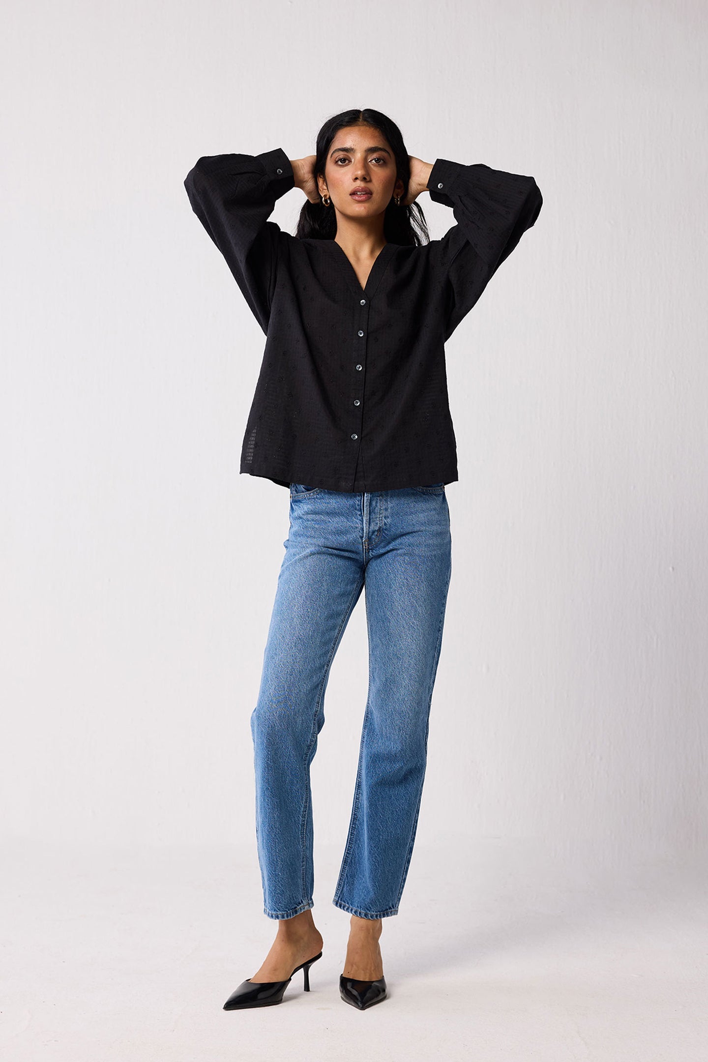 Woman wearing a black blouse and blue jeans against a white background