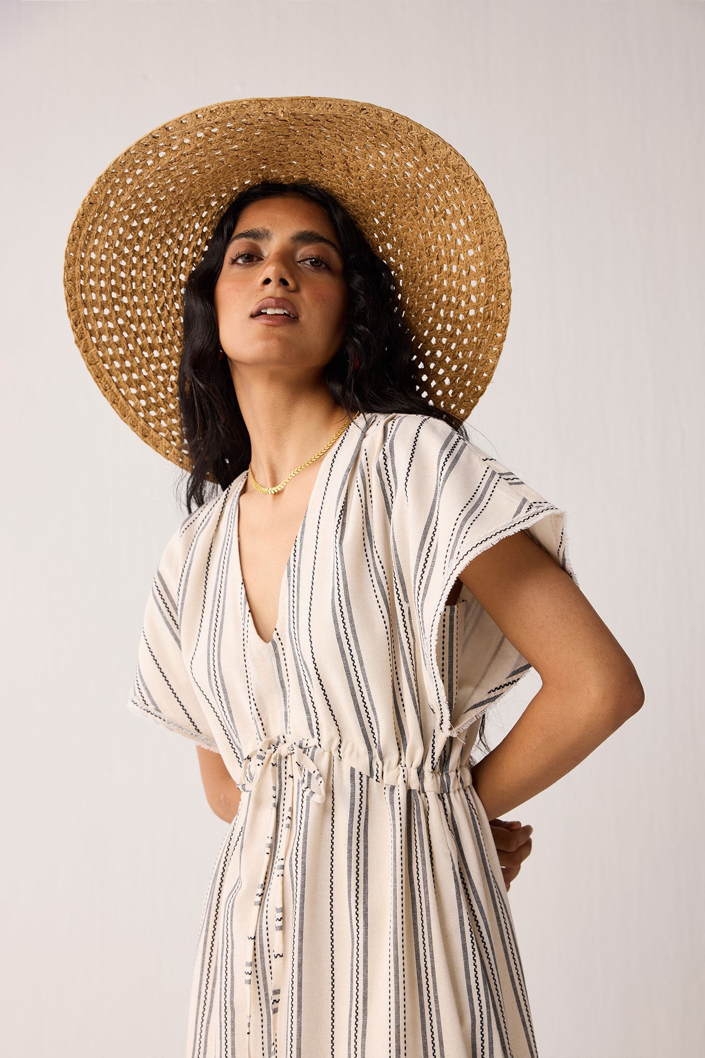 Woman wearing a striped dress and straw hat against a plain background