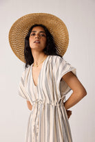 Woman wearing a striped dress and straw hat against a plain background